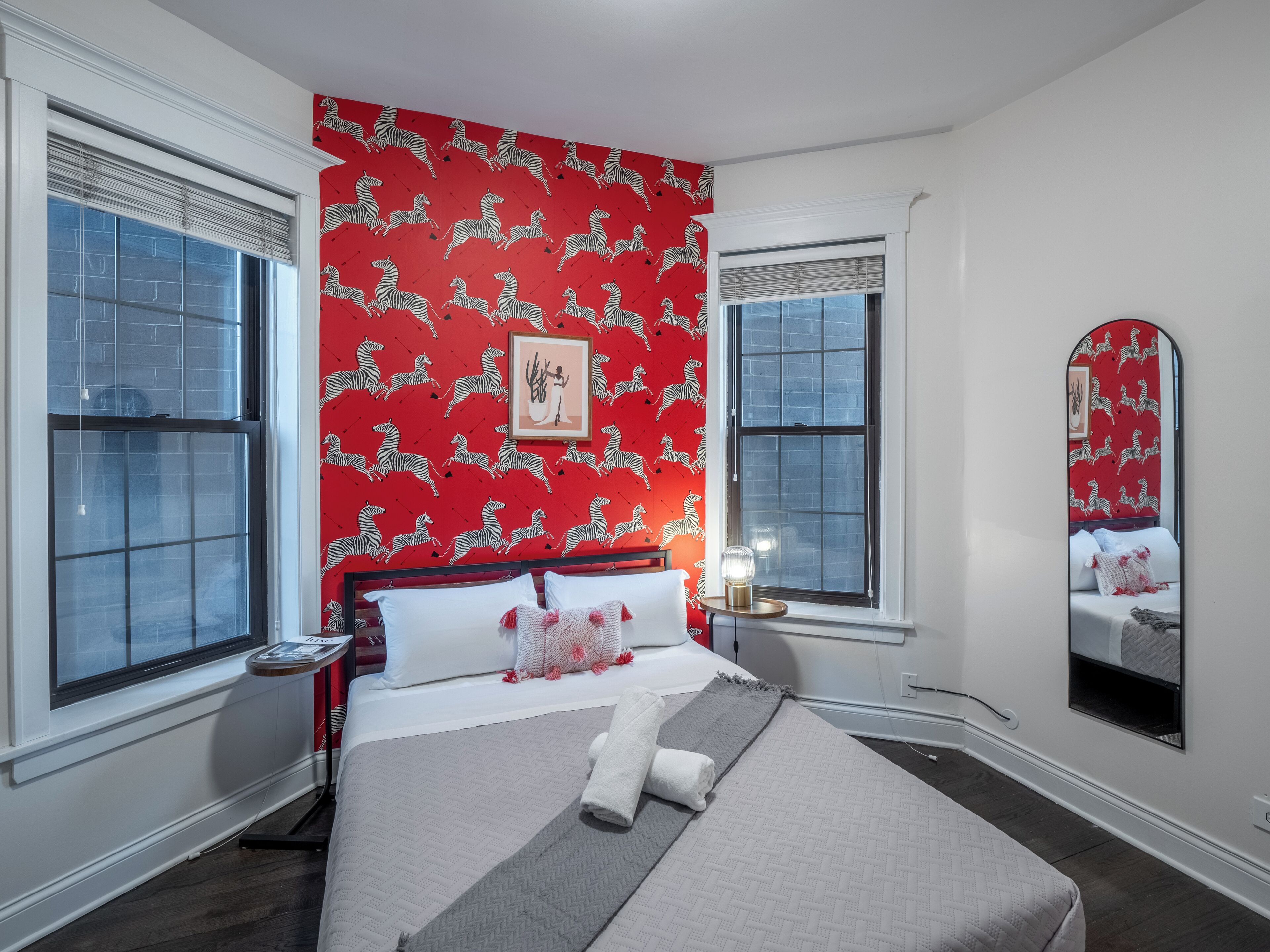 A hotel room with a large bed, two windows, a red zebra-patterned wall, and a mirror.