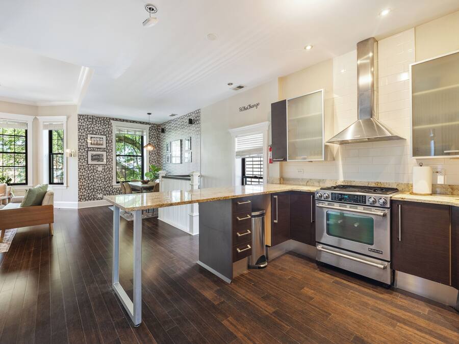 A modern kitchen with dark wood flooring, stainless steel appliances, and a large island with a glass top.