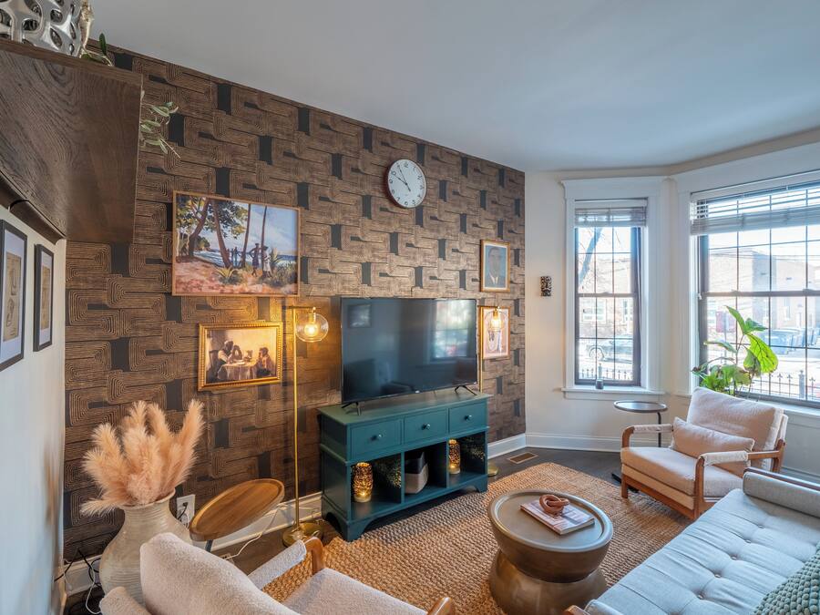 A living room with a patterned wall, a clock, a TV, and a window with a view.
