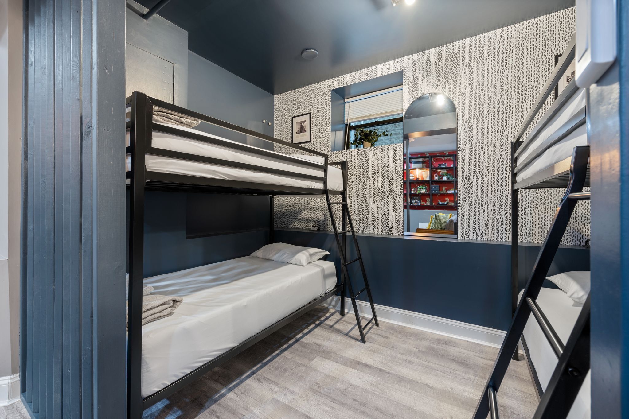 Une chambre avec un lit superposé, une fenêtre, un plancher en bois et une bibliothèque.