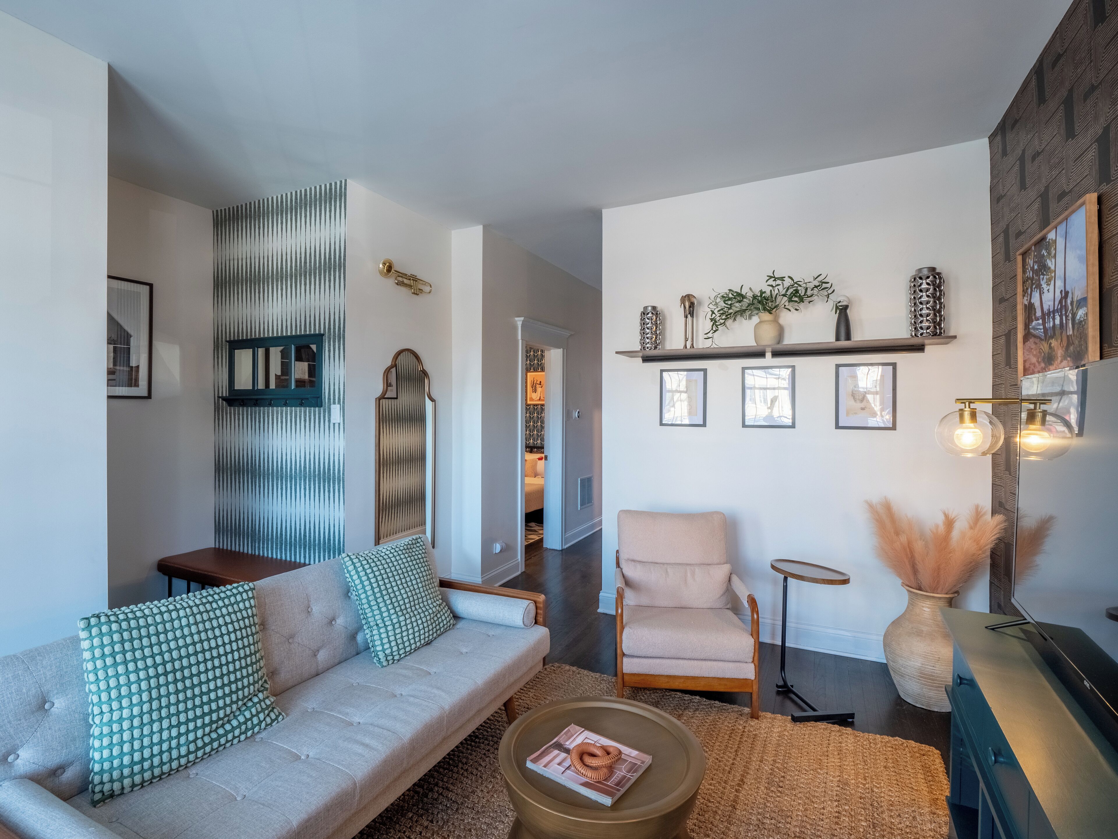 Ein modernes Wohnzimmer mit Sofa, Sessel und Couchtisch, einem Spiegel, dekorativen Regalen und einem Kamin.