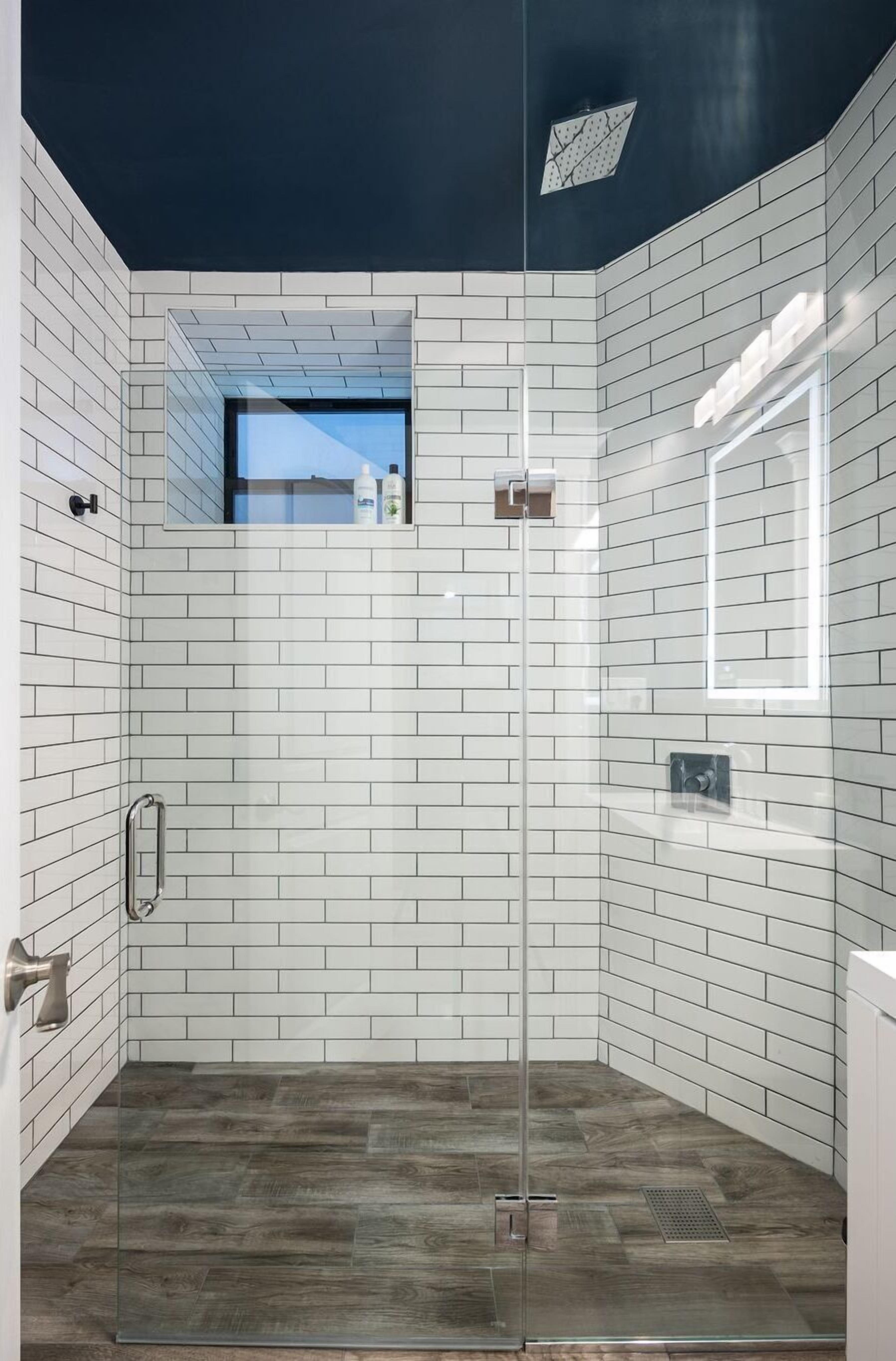 A modern shower room with white tiled walls, a glass door, and a wooden floor.