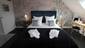 A bedroom with a large bed, two bedside tables with lamps, a desk with a chair, and a wall with a floral mural. - Domaine de Champouteau (Averdon)