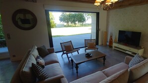 A living room with a sofa, armchair, coffee table, TV, and a door leading to a patio. - Domaine de Champouteau (Averdon)