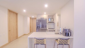 Eine moderne Küche mit weißer Arbeitsplatte, zwei Barhocker, einer Mikrowelle, einem Kühlschrank und einem Spülbecken.