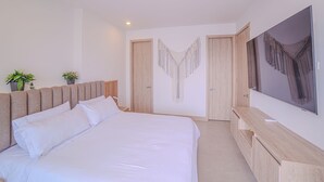 Ein modernes Schlafzimmer mit einem großen Bett, einem Holzkopfteil, einem Nachttisch, einem Fernseher und einem Kleiderschrank.
