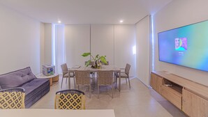 Ein modernes Wohnzimmer mit einer Couch, einem Esstisch, Stühlen, einem Fernseher und einer Pflanze.