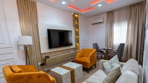 Una sala de estar moderna con un televisor de pantalla plana, sillones naranjas, un sofá beige y una mesa de centro de mármol.