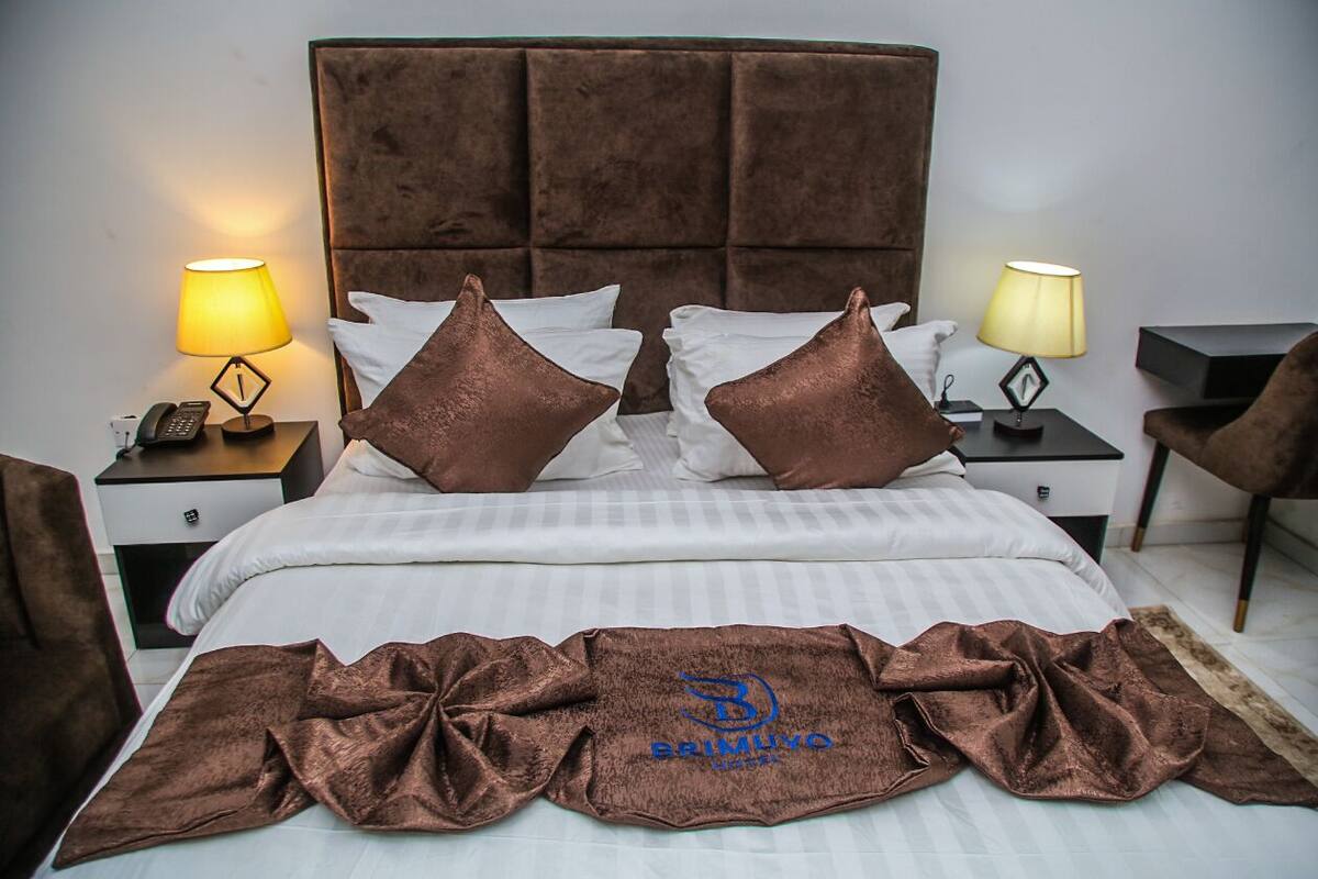 A neatly made bed with a brown headboard, two bedside lamps, and a brown throw blanket.