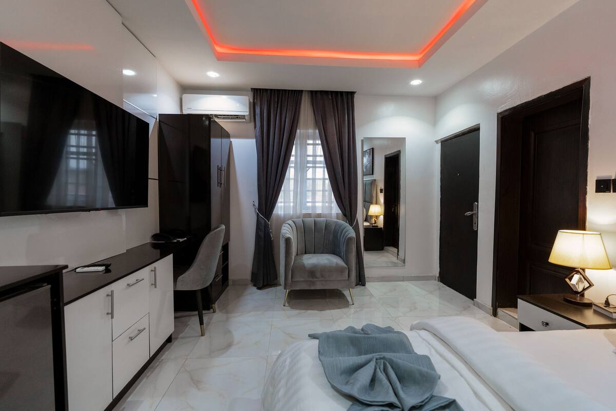 A modern hotel room with a bed, a desk, a chair, a TV, and a mirror.