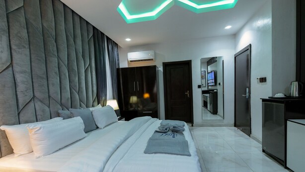 Una habitación de hotel moderna con una cama grande, un televisor de pantalla plana, un minibar y un baño con espejo y lavamanos.