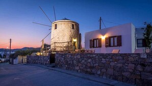 A stone-walled building with a round tower and a white building with wooden shutters.