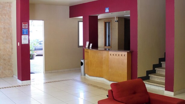 A hotel lobby with a reception desk, red seating area, and a staircase. - Hotel Virginia (Oaxaca)
