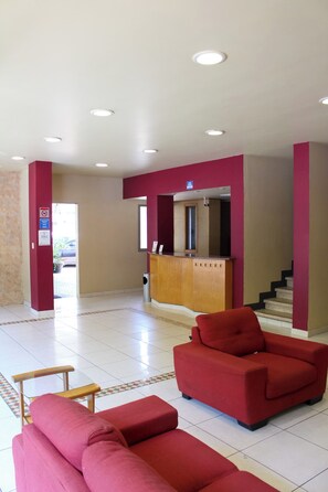 A hotel lobby with a reception desk, red seating area, and a staircase. - Hotel Virginia (Oaxaca)