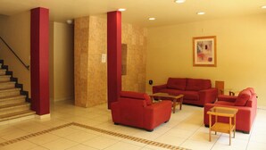 A spacious living area with red sofas and a wooden coffee table, a staircase with red accents, and a tiled floor. - Hotel Virginia (Oaxaca)
