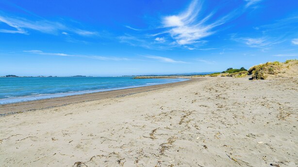 Un'ampia spiaggia sabbiosa con onde dolci, cielo azzurro limpido e rilievi all'orizzonte.