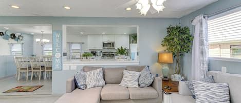 A modern living room with a sectional sofa, a dining area, and a kitchen in the background.