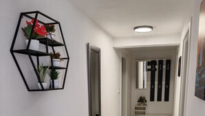A hallway with a geometric wall shelf holding plants, a mirror, and a door leading to another room. - Apartments Mihovilovi (Trogir)