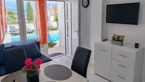 A modern room with a sofa, dining table, TV, and a view of a swimming pool. - Apartments Mihovilovi (Trogir)