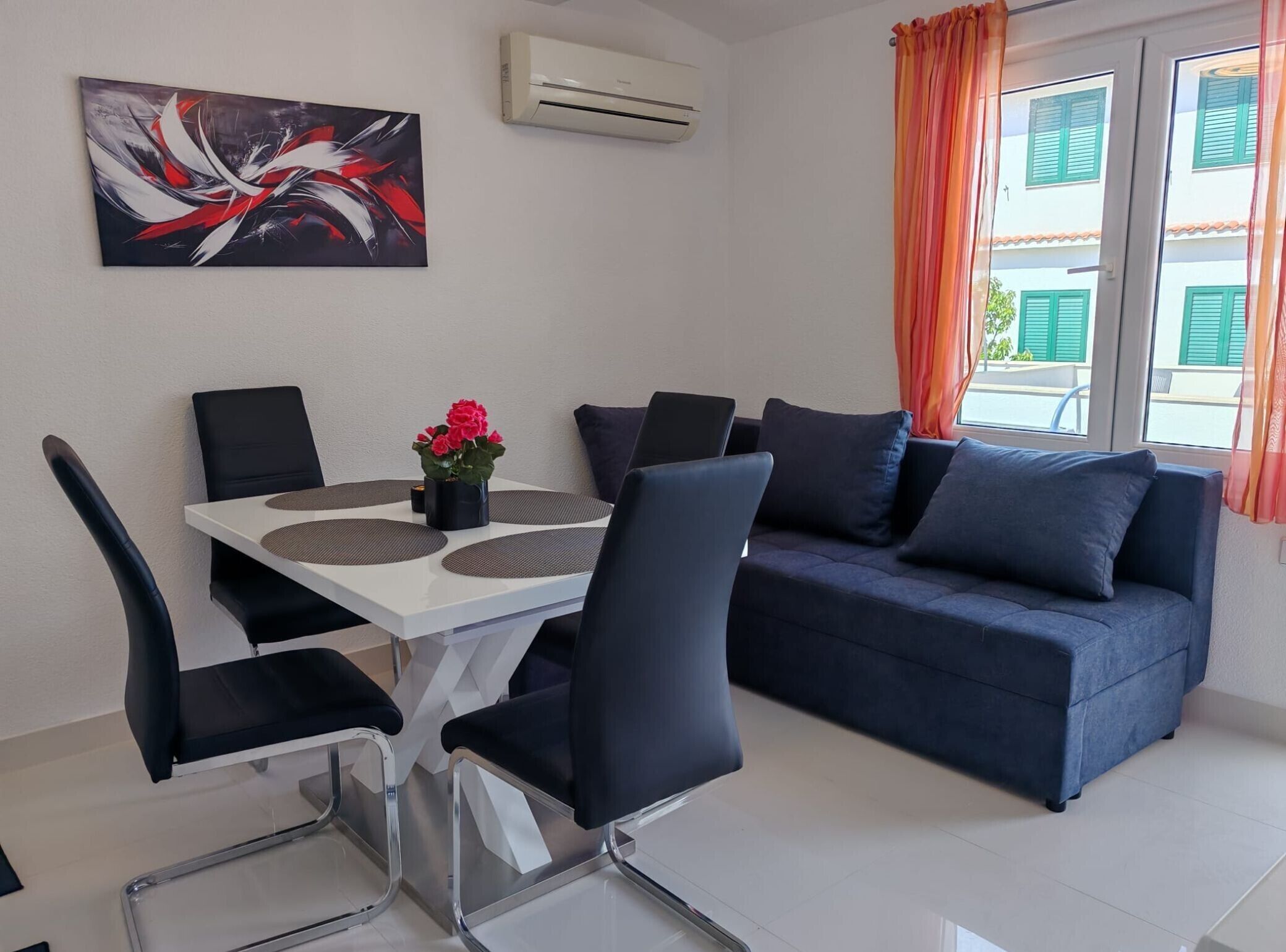 Un salon moderne avec une table à manger, des chaises noires, un canapé bleu et un tableau accroché au mur.