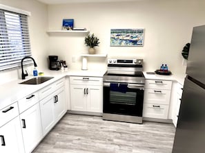 A modern kitchen with white cabinets, a stainless steel oven, a refrigerator, and a coffee maker.