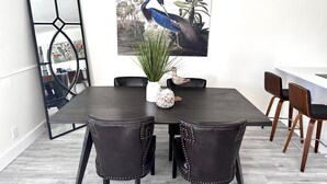 Ein Essbereich mit einem dunklen Holztisch, vier Stühlen, einer weißen Vase mit einer Vogelstatue und einem großen gerahmten Gemälde von einem Vogel und Pflanzen an der Wand.