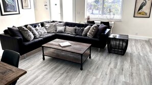 Ein modernes Wohnzimmer mit einem Ecksofa, einem Holztisch und einem schwarzen Korbwäschesammler.