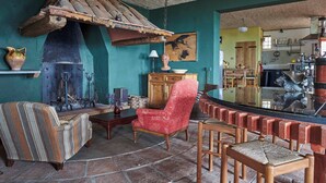 Un interior rústico con chimenea de piedra, un sillón rojo y una zona de bar de madera.