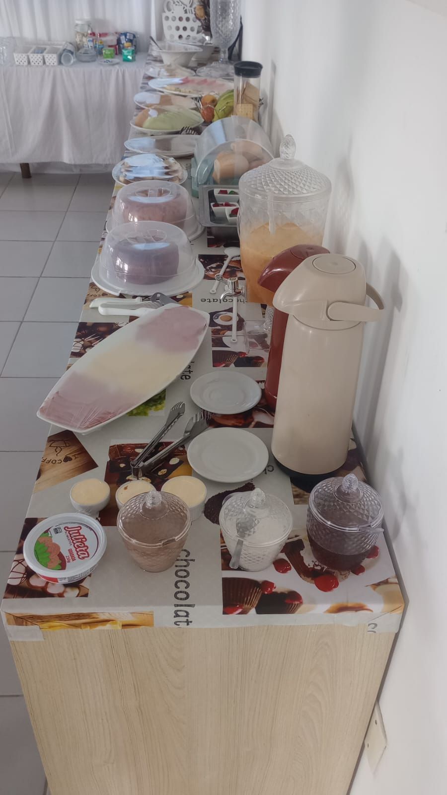 Una mesa de bufé con diversos alimentos y recipientes, incluyendo una jarra grande y varios platos cubiertos.