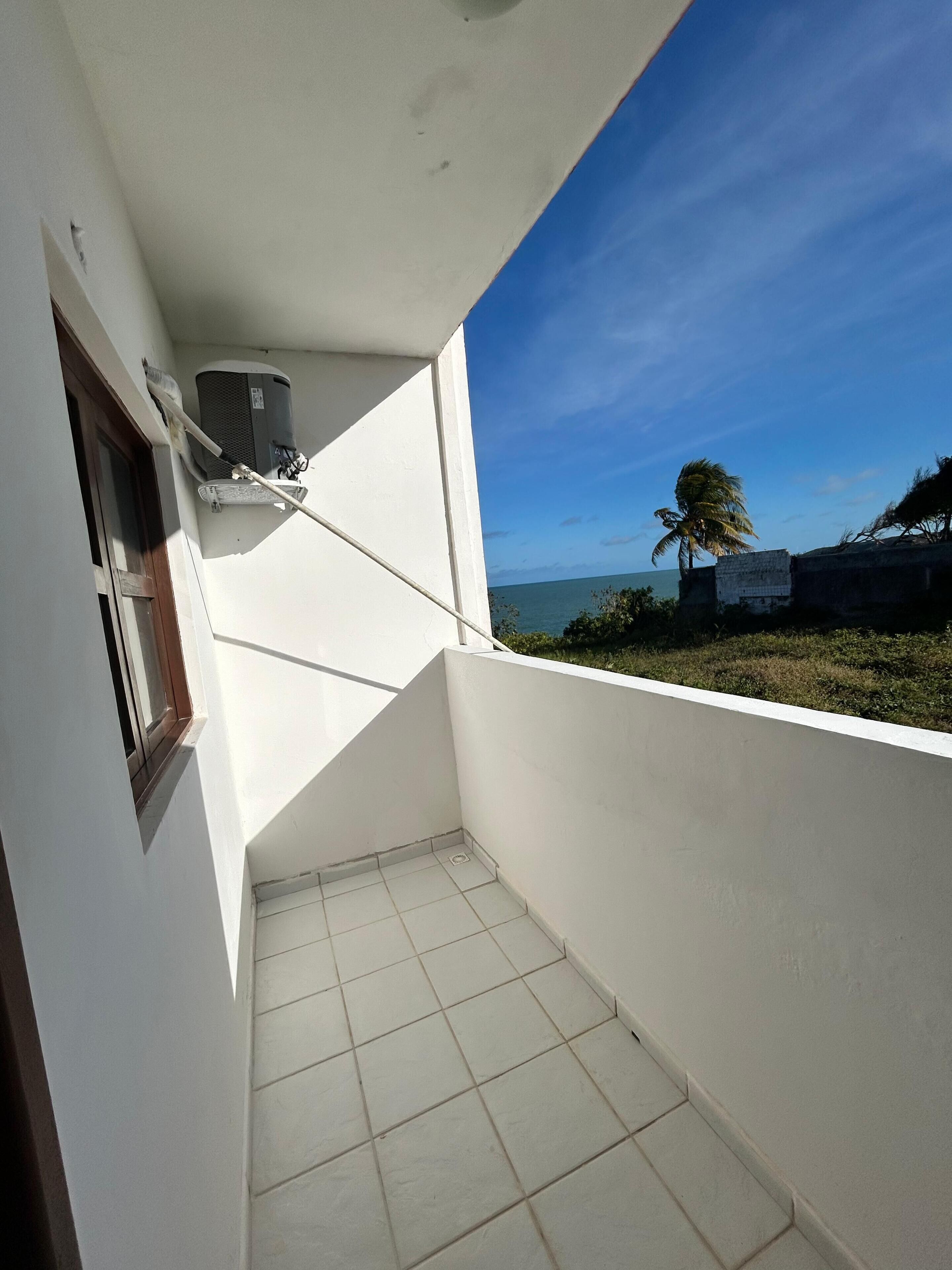 A small balcony with a tiled floor, a window, and an air conditioning unit.