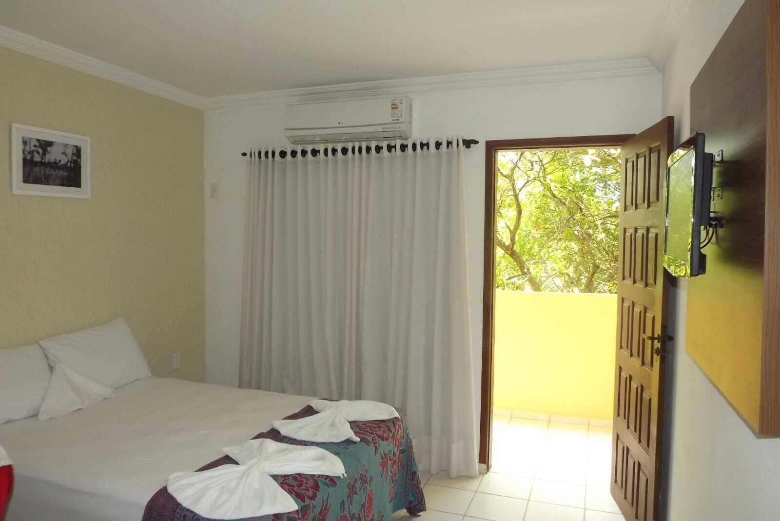Habitación de hotel con cama, ventana con cortinas, unidad de aire acondicionado y puerta que da a un área exterior.