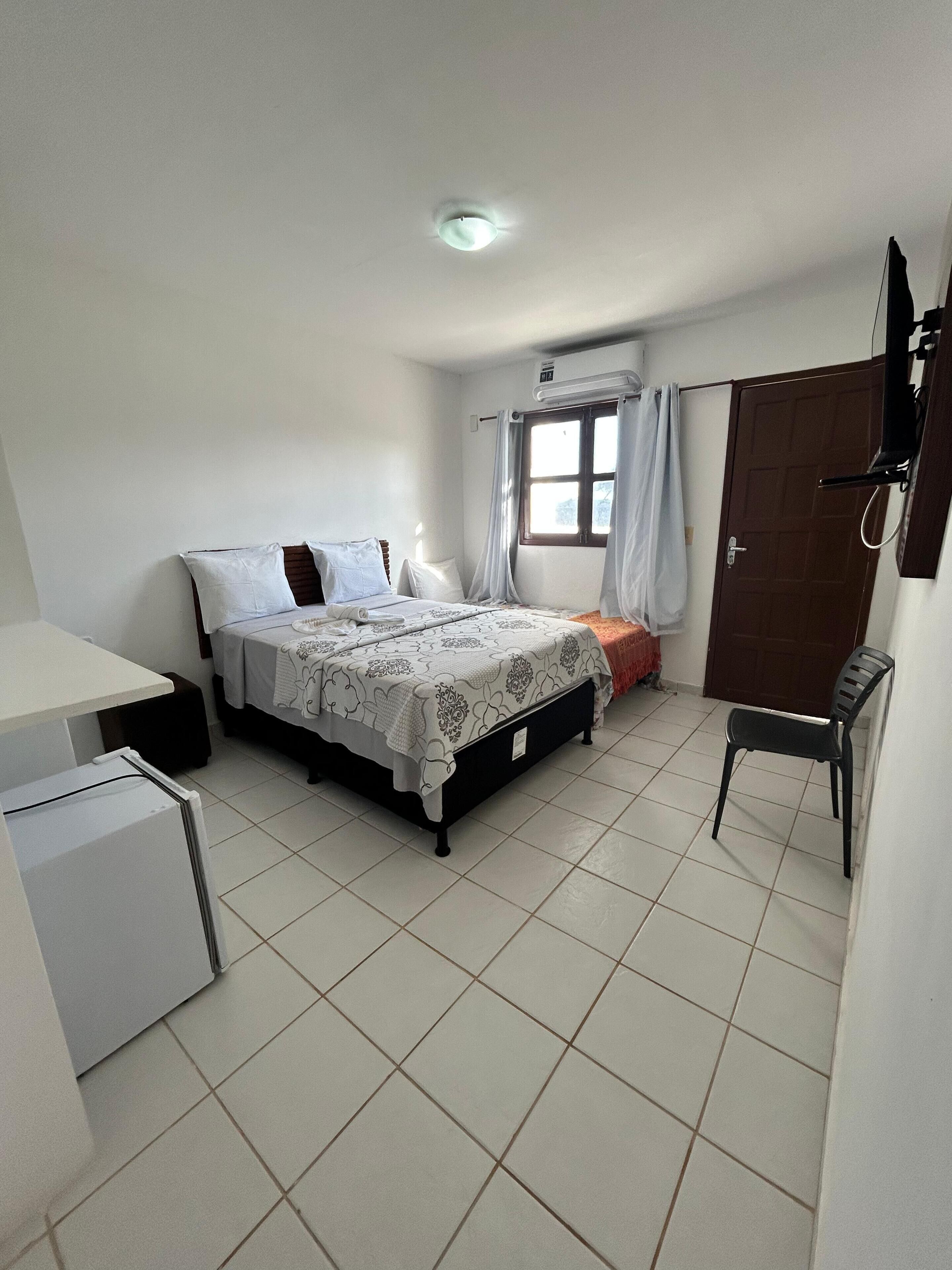 Un dormitorio pequeño y limpio con cama, escritorio, silla y ventana con cortinas.