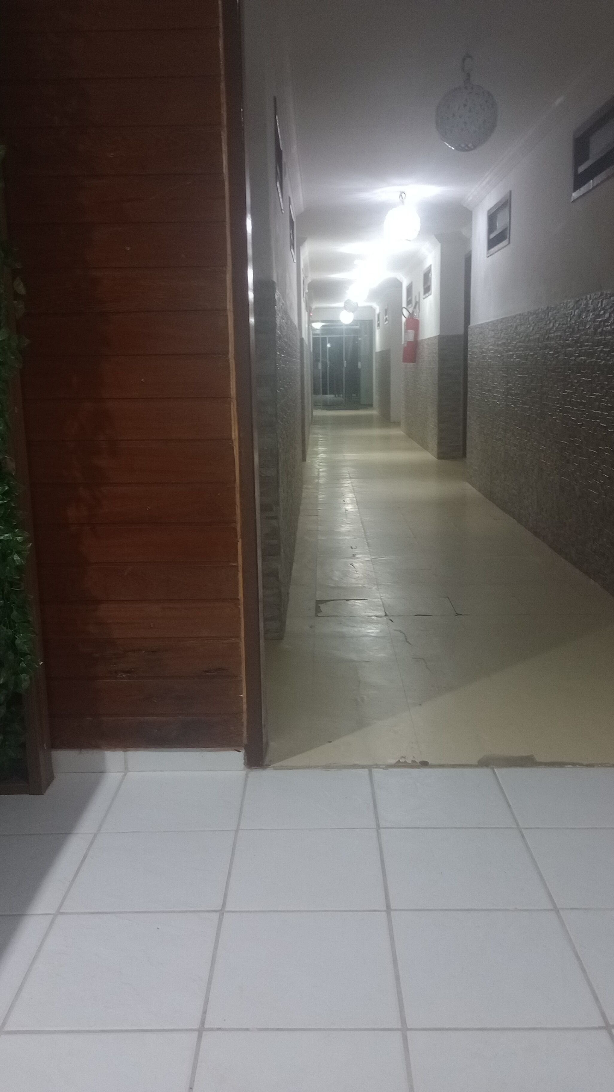 A hallway with tiled flooring, wooden walls, and a ceiling light fixture.