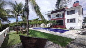 Una casa de dos pisos con piscina, mobiliario exterior y palmeras.
