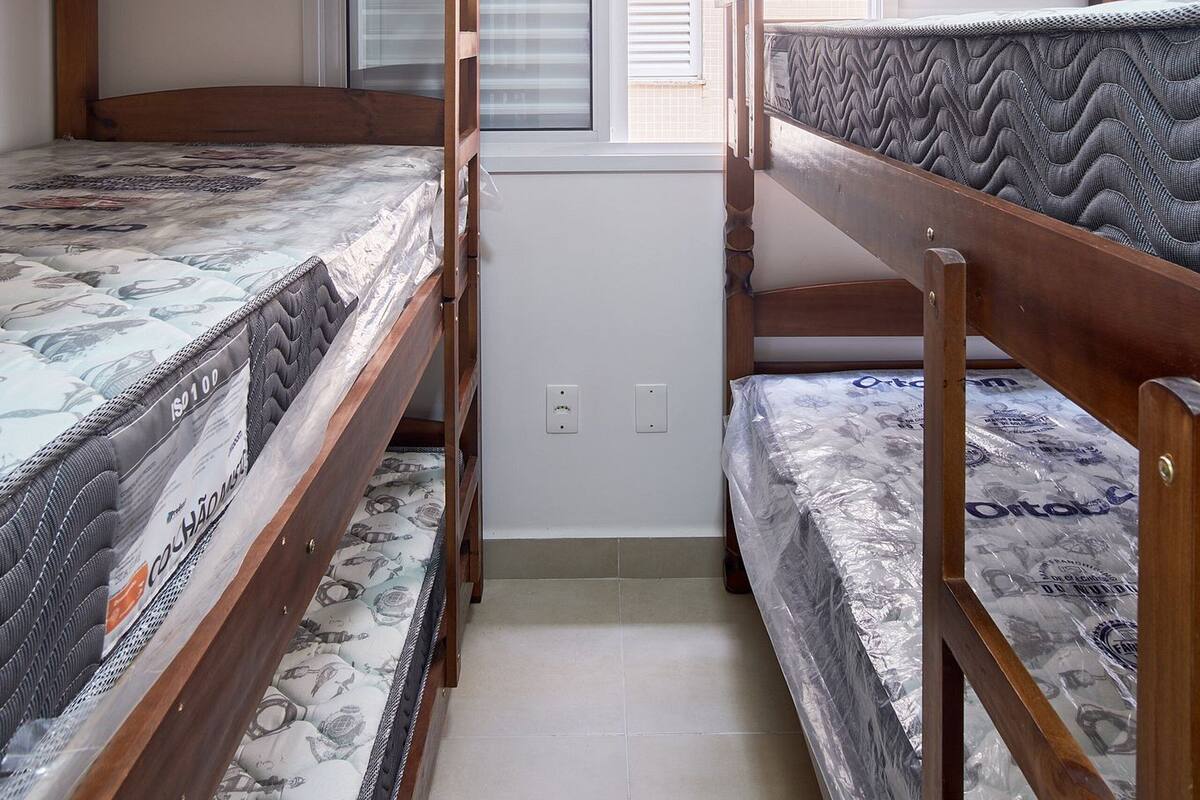 A room with two bunk beds, a window with blinds, and a tiled floor.