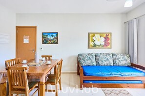 A room with a wooden dining table, chairs, a bed with a blue mattress, and two framed pictures on the wall. - Residencial Saint Barth (Ubatuba)