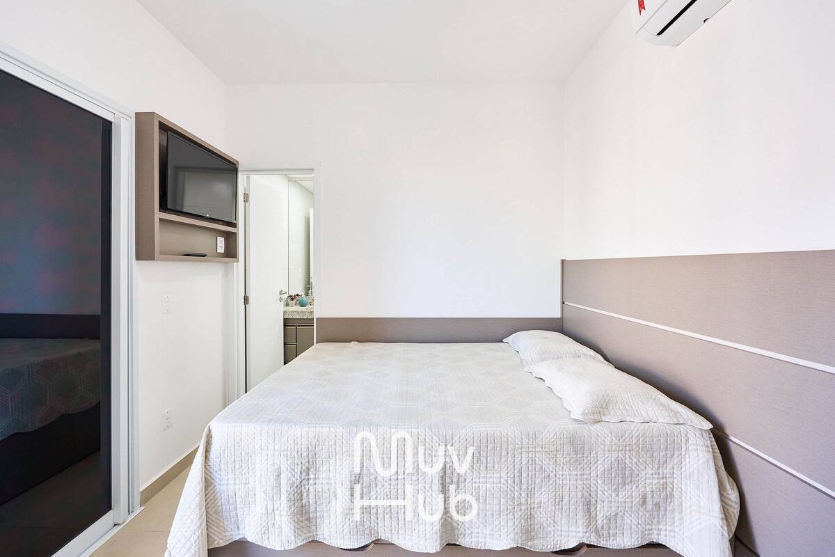 A bedroom with a bed, a television mounted on the wall, and a sliding door leading to another room.