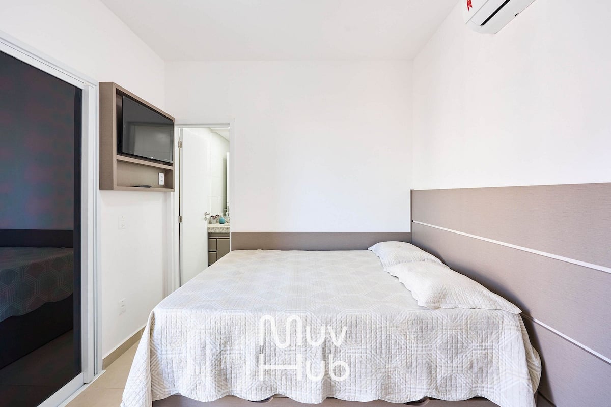 Un dormitorio con una cama, un televisor montado en la pared y una puerta corredera que da a otra habitación.