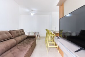 Una sala de estar con un sofá marrón, un televisor, sillas amarillas y una mesita.
