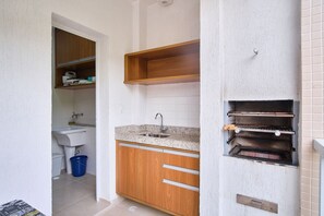 A compact kitchen with a sink, wooden cabinets, and a built-in oven. - Residencial Saint Barth (Ubatuba)