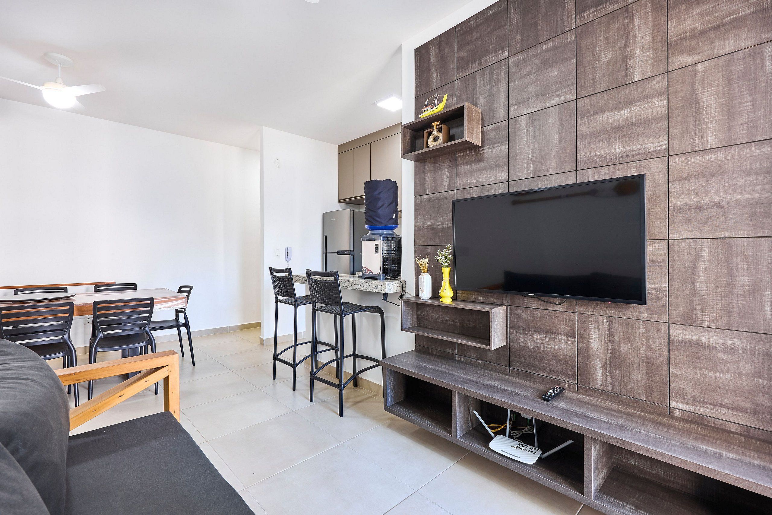 Una sala moderna con televisor de pantalla plana montado en una pared de madera, un comedor con mesa y sillas, y un sofá.