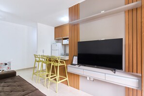 A modern living room with a flat-screen TV, wooden panel wall, yellow chairs, and a white sofa. - Residencial Saint Barth (Ubatuba)