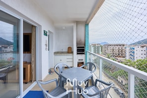 Un balcón con mesa y sillas, un ventanal corredero, una zona de cocina y vistas a la ciudad.