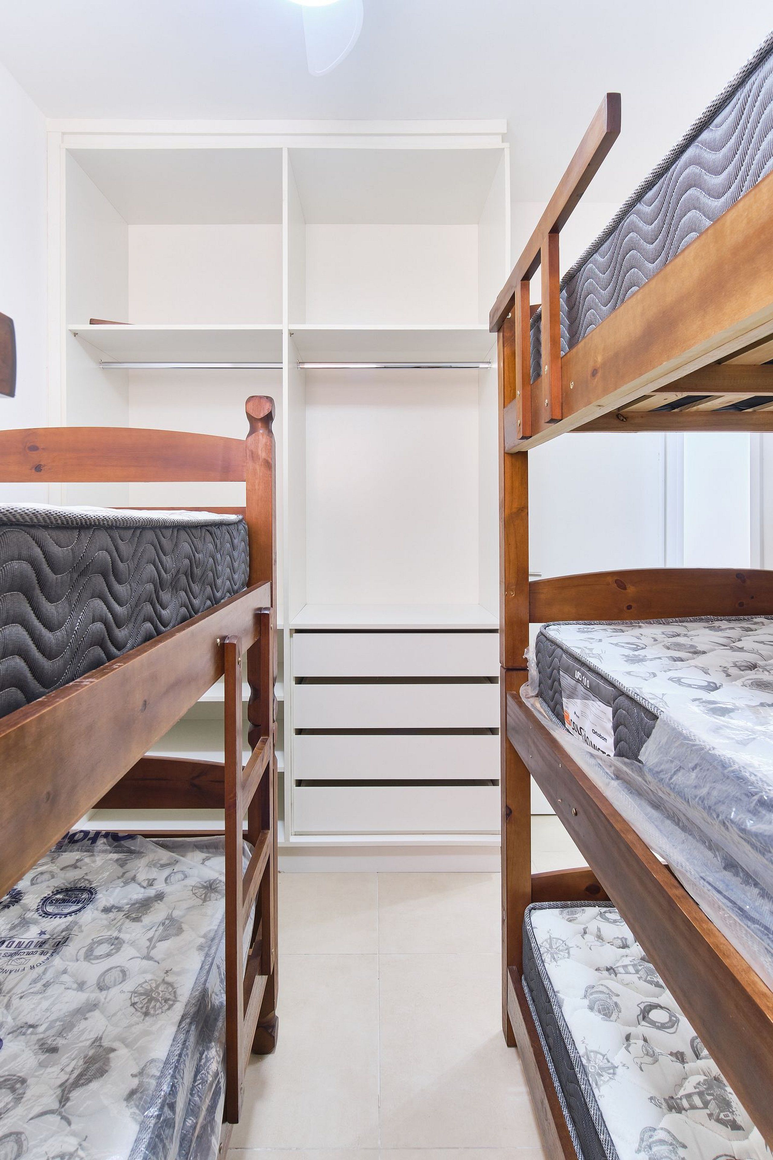 Ein Zimmer mit Etagenbetten, einem weißen Kleiderschrank und Fliesenboden.