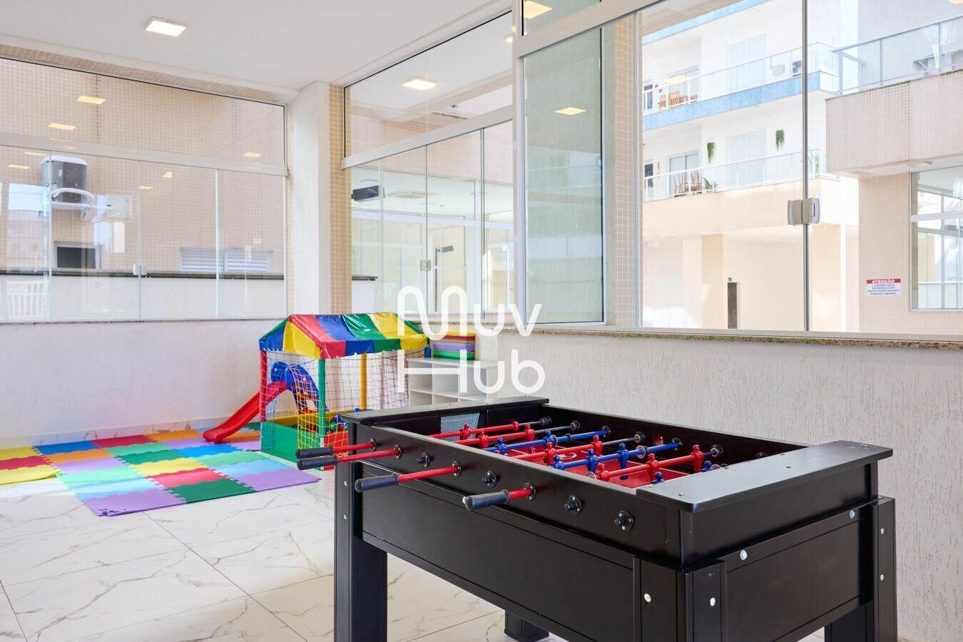 Een tafelvoetbaltafel en een kleurrijk speelgedeelte in een hotel lobby met grote ramen en uitzicht op het interieur van het gebouw.