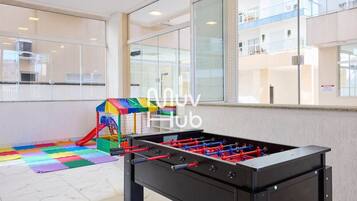 Een tafelvoetbaltafel en een kleurrijk speelgedeelte in een hotel lobby met grote ramen en uitzicht op het interieur van het gebouw.