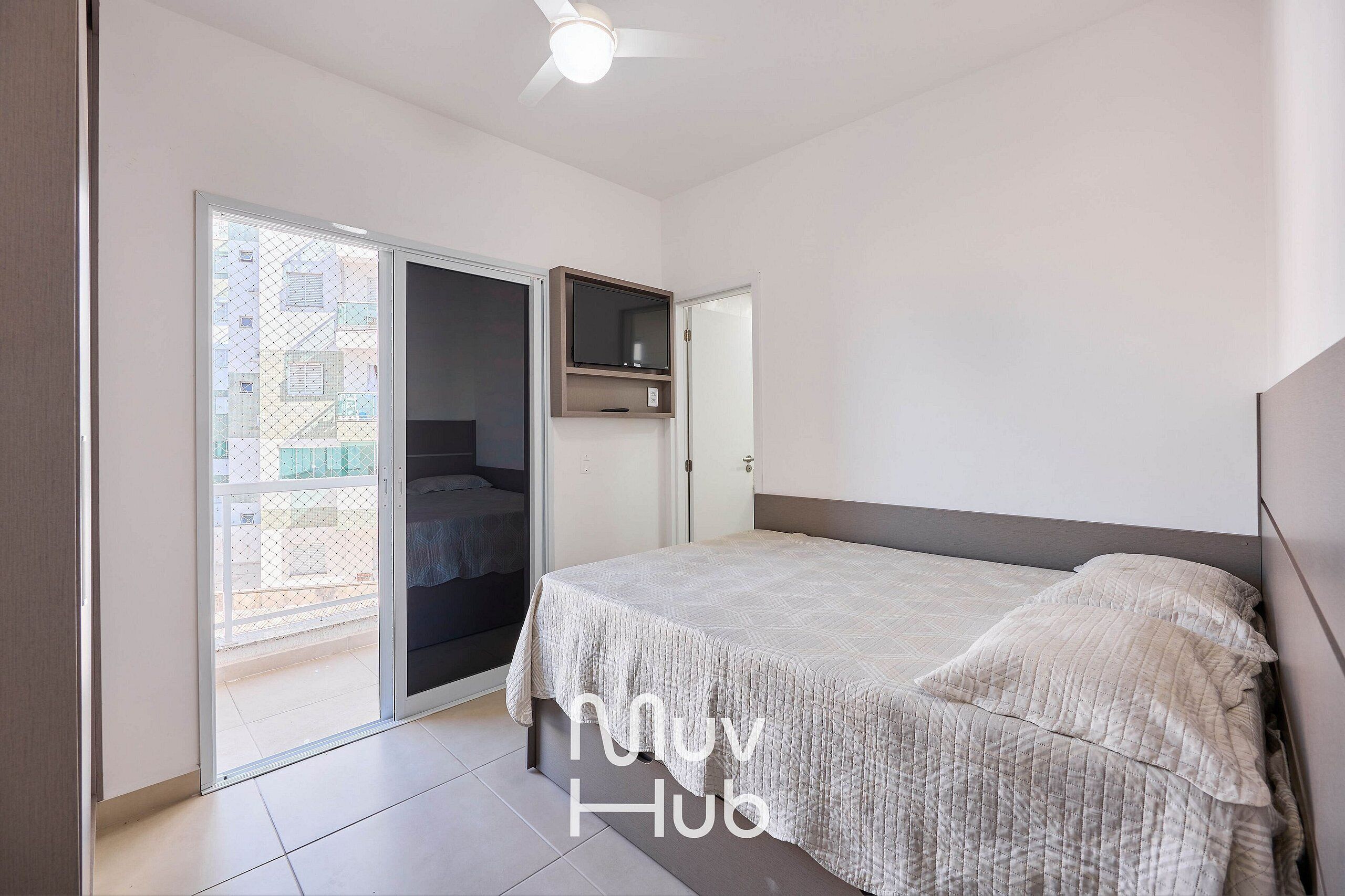 Une chambre à coucher avec un lit, un ventilateur de plafond et une porte coulissante donnant sur un balcon.