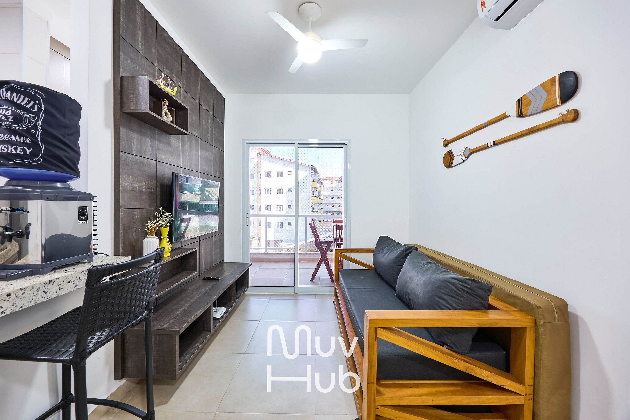 Una sala moderna con un sofá, una mesa de centro de madera, un televisor y un comedor con un banco y una pequeña mesa.