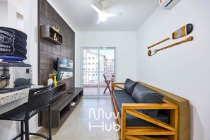 A modern living room with a sofa, a wooden coffee table, a TV, and a dining area with a bench and a small table. - Residencial Saint Barth (Ubatuba)