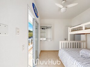 Un dormitorio infantil con literas, ventilador de techo y armario con ropa colgada.